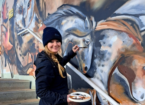 A painter painting a lovely mural of some horses and a barn owl
