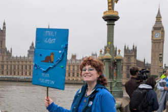 Photo of a member of staff in front of the houses of parliament with a sign for the march for clean water