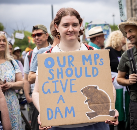 Young person holding a sign saying 'our MPs should give a dam' with a drawing of a beaver