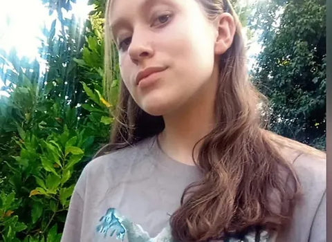 A young girl looking into the camera with a green leafy background